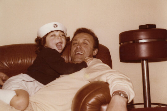 1981. Father and son playing and laughing on the sofa.