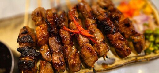 Homemade beef Satay marinated with spice and sweet soy sauce, coriander beef satay, served on plate with onion, chilli, soy sauce and tomato