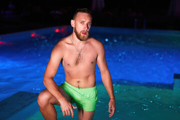 Seductive homosexual man celebrating gay pride with at night LGBTQ pool party in a private villa swimming pool. Bisexual male in swimwear posing on camera.