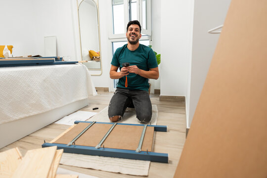 smiling man looking at the camera while assembling furniture