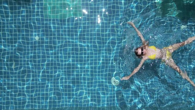 Top view of young caucasian woman swimming on the back in the pool in slow motion.