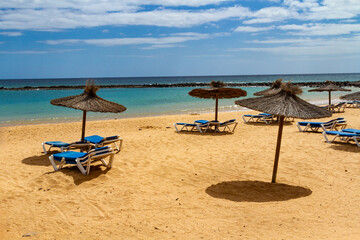 An empty beach in the off-season with straw umbrellas and blue sun lounger.  Playa del Castillo in ...