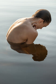 Wet topless model reflected on water surface while posing outdoo