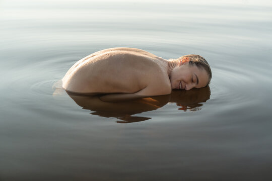 Wet topless model reflected on water surface while posing outdoo
