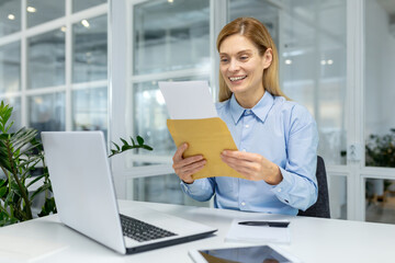 Smiling professional woman reading a letter, expressing joy and satisfaction at her office...