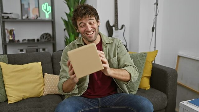 A cheerful man holds a package in a cozy living room, expressing excitement and satisfaction with his delivery.