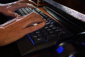 Illuminated keyboard with man's hands typing on a computer: concept of hacker or programmer working in a technological environment, on black background