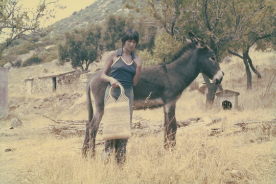 1974. A young woman poses for a photo next to a donkey.