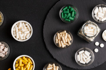 Various vitamins, minerals and dietary supplements in jars from above on a black stone desk on a black background. Pills, tablets and capsules flat lay. Healthy lifestyle.