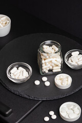 White colored nutritional supplements  in jars on a black desk on a black background. Vitamins and...