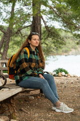 Obraz premium The traveler with a backpack rests on a bench in the forest by the sea.