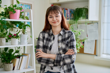 Portrait of smiling female teenager looking at camera with crossed arms in home
