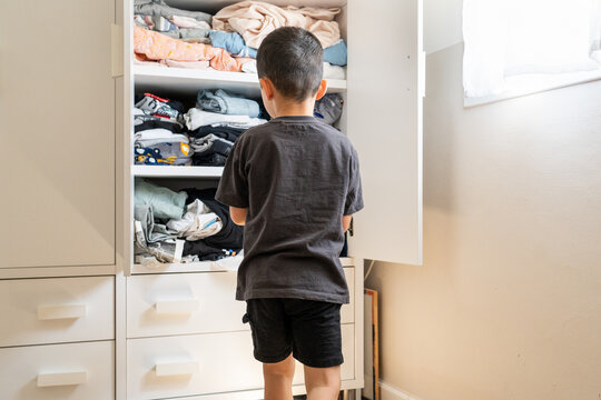 Young Boy Selects Wooden Wardrobe Outfit in Sunlight.