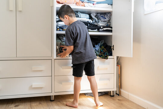 Young Boy Organizes Clothes in Open Wardrobe.