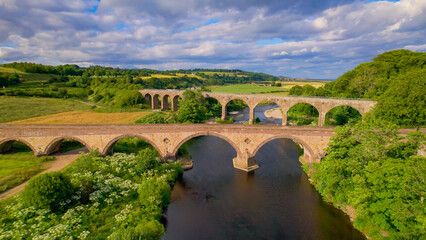 Fototapeta na wymiar AERIAL: Picturesque Scottish landscape and two old stone bridges crossing river
