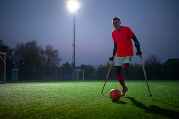 Legs of disabled football plaer with ball and crutches.