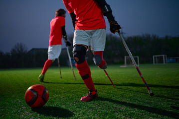 Legs of disabled football plaer with ball and crutches.