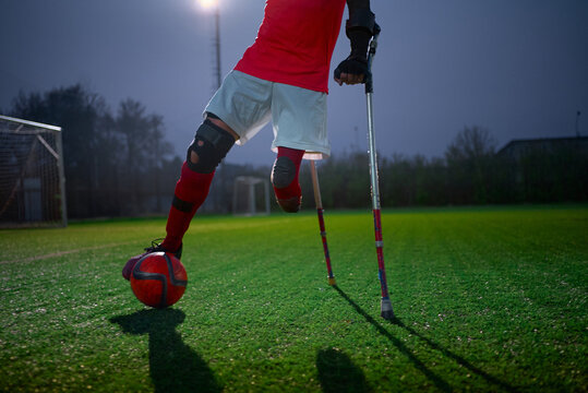 Legs of disabled football plaer with ball and crutches.