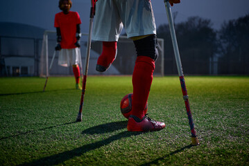 Legs of disabled football plaer with ball and crutches.