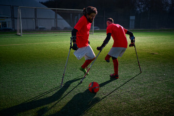 Legs of disabled football plaer with ball and crutches.