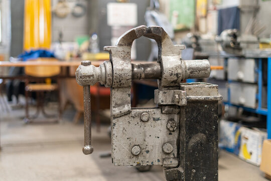 An old, worn, gray-painted large vise on a stand in the middle of an empty welding shop