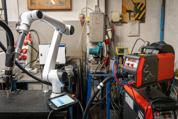 A modern welding robot in an old crowded welding workshop