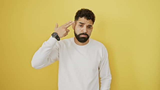 Frustrated young man, standing and gesturing suicide, pointing finger-gun to his head over isolated yellow background