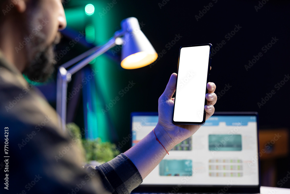 Poster man vertically holding mobile device with isolated copyspace mockup template. in front of a laptop s