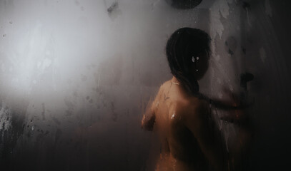 A contemplative moment as a silhouette of a person is seen through the foggy, steamed-up glass of a shower.