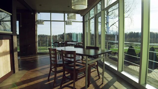 Simple Country Inn Dining Room Interior. Behind the Window View of the Golf Course. The Evening Sun is Shining. The Interior is Simple with Tables and Chairs.