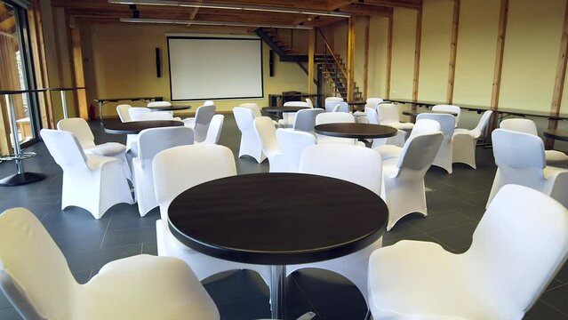 Arranged Tables with Chairs in the Hotel Hall. Small Round Tables and Chairs Upholstered in White Fabric. Team Building Events Can Take Place in Such a Room.