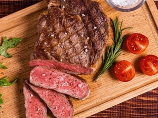 Grilled barbecue meat served sliced on the board with tomatoes and herbs