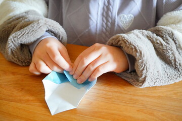 小学生の子供が折り紙を折っている手元。小学4年生、10歳。 - obrazy, fototapety, plakaty