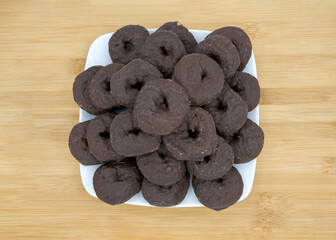 close up on a square plate with round chocolate donuts on a light wood table.