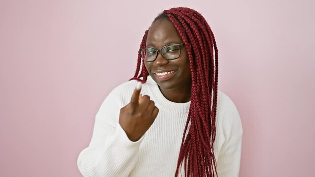 African american woman with braids wearing glasses and a white sweater beckoning against a pink background.