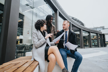 Obraz premium A multicultural group of people engage in a business discussion outside an office building, reviewing documents together.