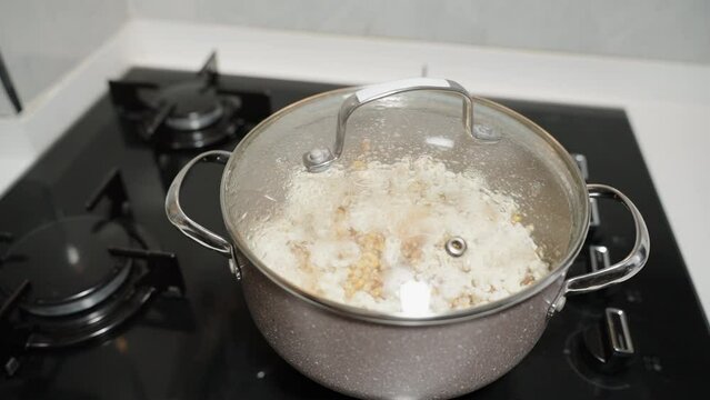 On the gas stove, a pot with popping popcorn, circular view in slow-motion.