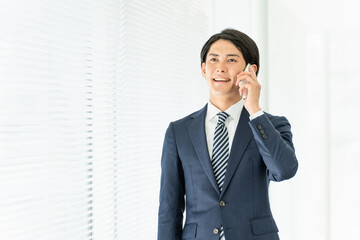 スマホで電話・通話するスーツ姿の若いアジア人男性ビジネスマン
