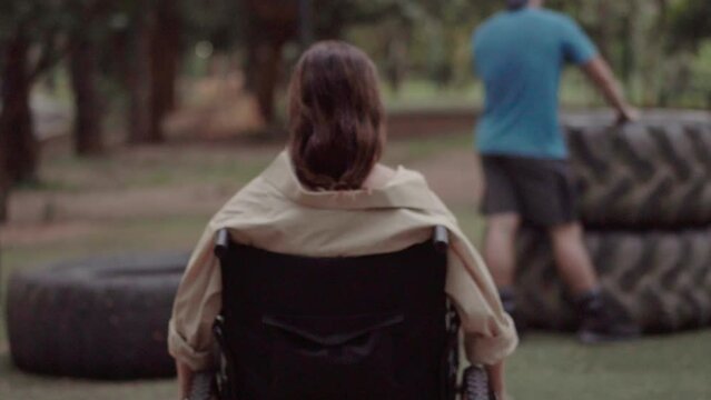 A disabled girl in a wheelchair moves a lever. In the park during the day