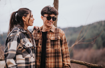 A young couple in stylish plaid jackets shares a close, joyful moment together outdoors, embodying...