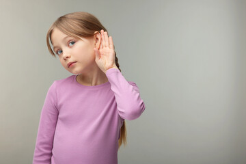 Little girl with hearing problem on grey background. Space for text