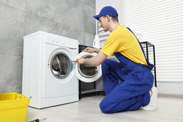 Plumber repairing washing machine in bathroom, low angle view