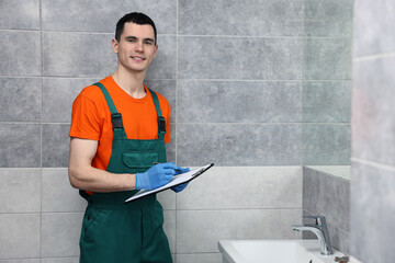 Young plumber writing results of examining sink in bathroom