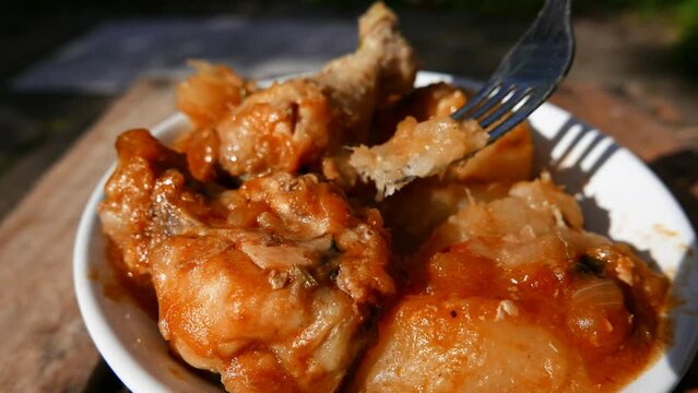 Person eating cooked chicken with boiled cassava and onion sauce (POV, top view). Plate of food. Close-up shot: a hot lunch plate in the sun. Person having lunch. Boiled manioc and hot chicken pieces.
