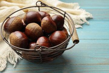Roasted edible sweet chestnuts in metal basket on light blue wooden table, closeup. Space for text
