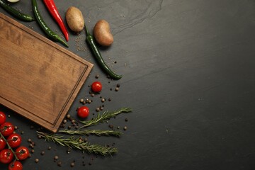 Cooking concept. Wooden cutting board and different products on black table, flat lay. Space for...