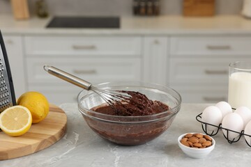 Metal whisk, chocolate cream in bowl and different products on gray marble table indoors