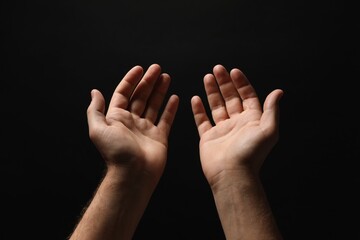 Religion. Man with open palms praying on black background, closeup