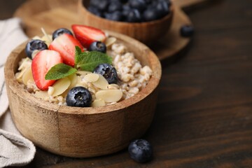 Tasty oatmeal with strawberries, blueberries and almond flakes in bowl on wooden table, closeup....