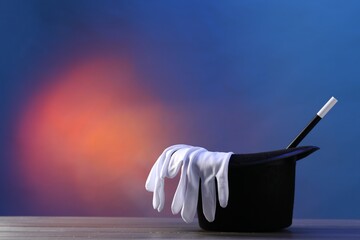 Magician's hat, wand and gloves on wooden table against color background, space for text